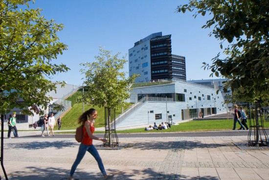 Kvinnelig student krysser en solrik campus med moderne universitetsbygning i bakgrunnen.