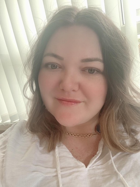 ung kvinne med bølget hår, i hvit bluse og med smilende munn