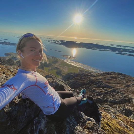 Ung dame som tar bilde av seg selv med fjell og solnedgang i bakgrunnen.