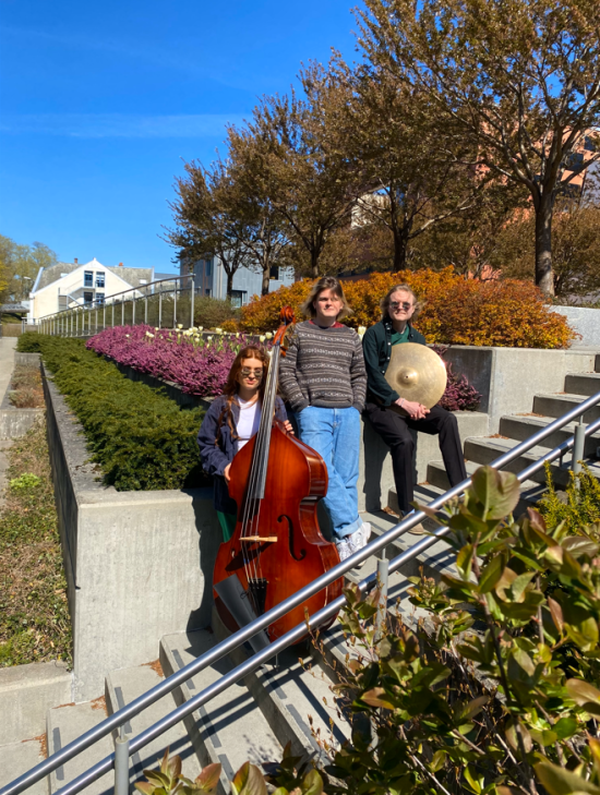 Pressebilde Regnsjekk. Adriana Døsvik med kontrabass, sammen  med Erlend Johannessen og Bendik Brochs i en trapp foran blomster