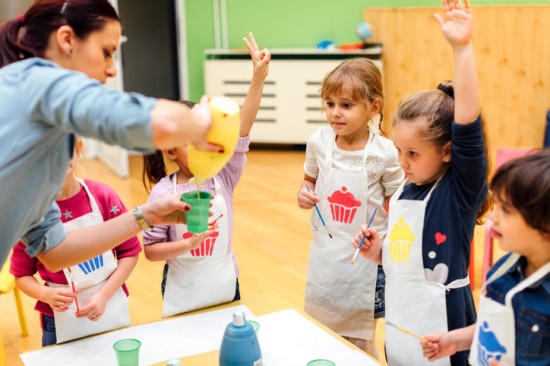 Kvinnelig barnehagelærer hjelper en gruppe barn med å male