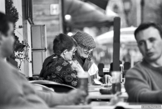 En eldre mann og dame leser avis på kafe.