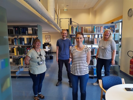 Fire kvinner og en mann står i bibliotek omgitt av bokhyller