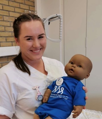 Kvinnelig jordmorstudent i uniform som holde en babydukke