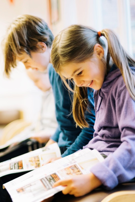 Gutt og jente i barneskolealder sitter ved siden av hverandre og leser hver sin avis