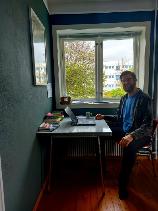 Sander Eriksen Mathisrud sit med ein open laptop ved eit kjøkkenbord. Han smiler mot kamera.