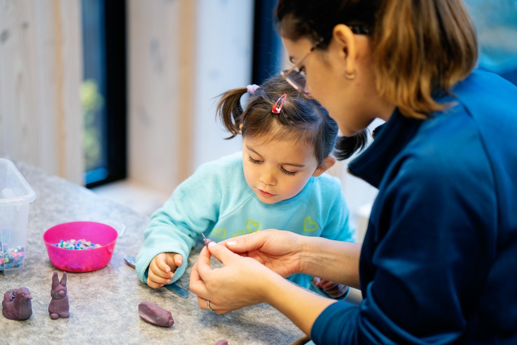 Kvinnelig barnehageansatt hjelper liten jente i barnehage med et kunst- og håndverksprosjekt