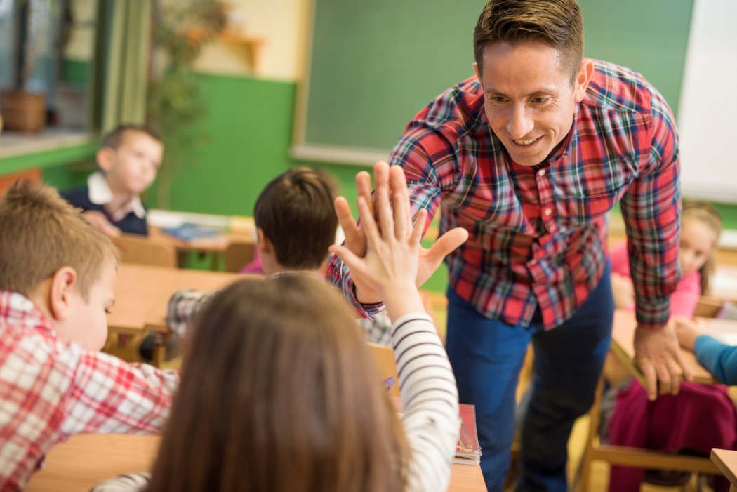 Mannlig lærer i klasserommet gir en high five til en elev