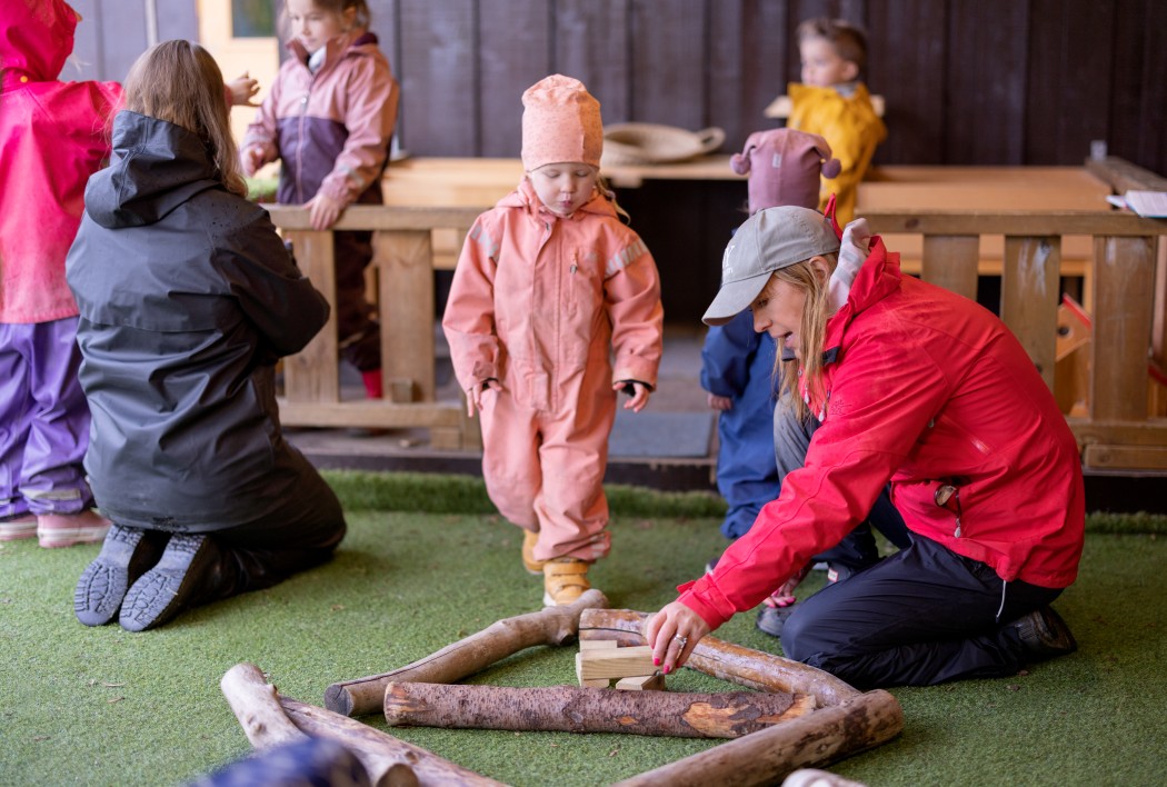 Barn og voksne i barnehage leker med greiner.