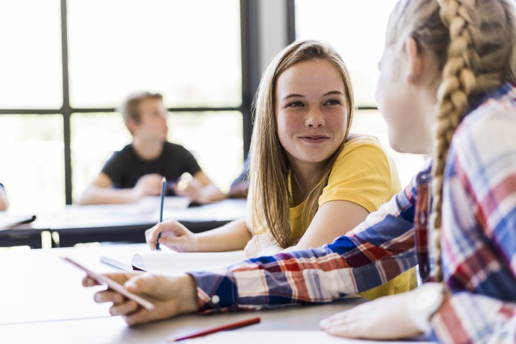 Jenter smiler til hverandre mens de gjør skolearbeid