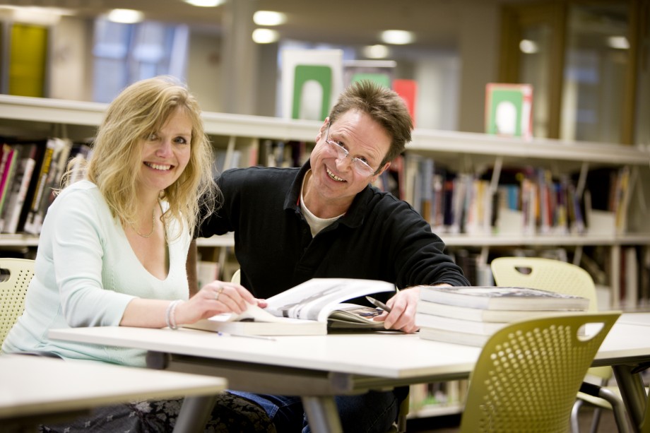 Kvinne og mann sitter sammen ved et bord i et bibliotek og studerer