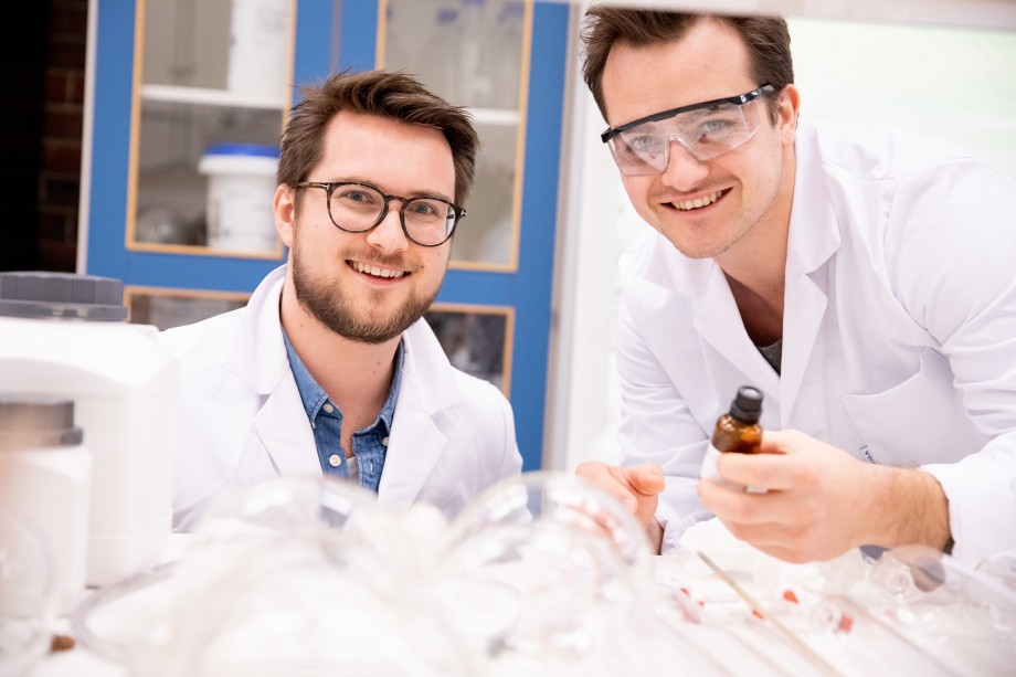 To mannlige studenter i labfrakk jobber på et laboratorium