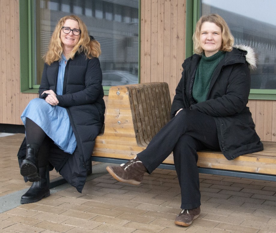 To kvinner sitter på en benk foran en bygning