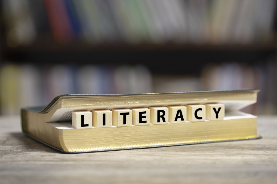 Halvåpen bok med en rekke bokstavterninger som staver literacy.