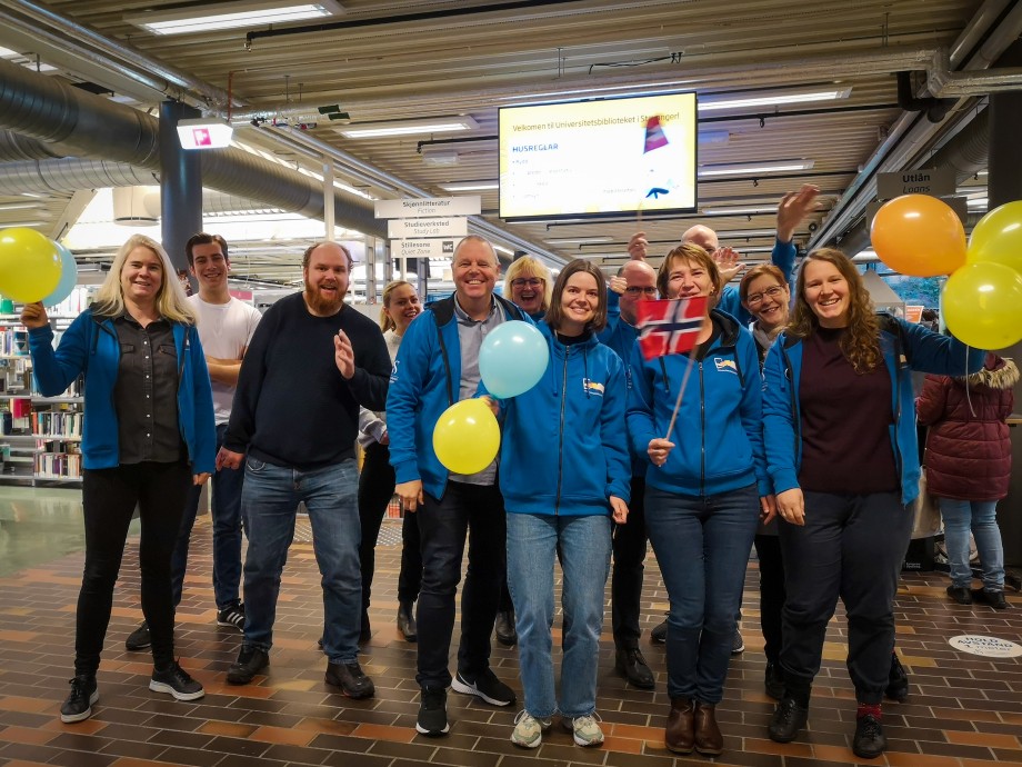 En gruppe mennesker smiler og feirer med ballonger og norske flagg