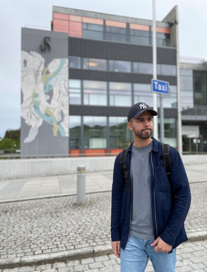 Ung mann med caps og mørk jakke står utenfor Arne Rettedals hus på UiS campus Ullandhaug