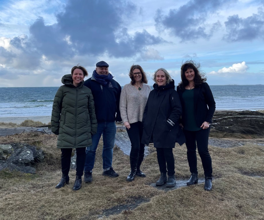 Fem medlemmer i en prosjektgruppe avbildet på en strand. 