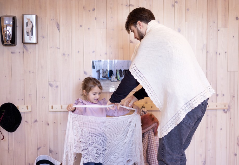 Mannlig barehagelærer holder opp en heklet duk foran liten jente. 