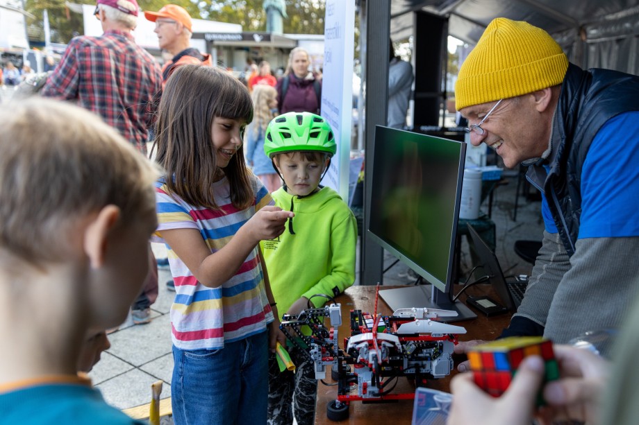 Jente og gutt ser på legorobot sammen med smilende mann