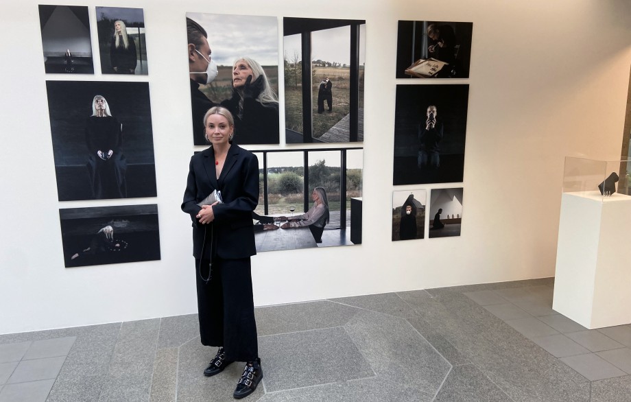 Woman dressed in black in front of a wall filled with art.