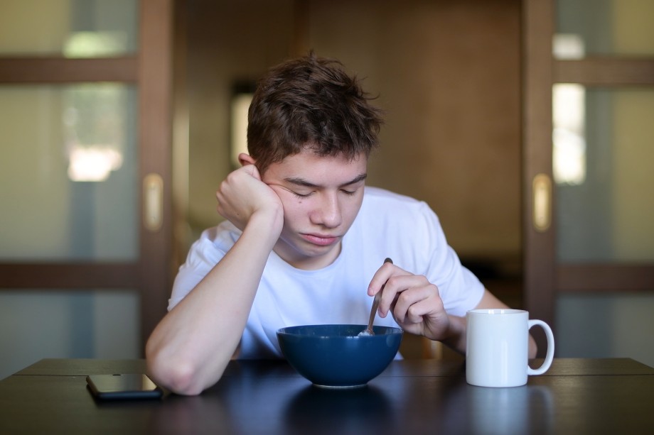 Søvning tenåring ved bord, foran skål og kaffekopp