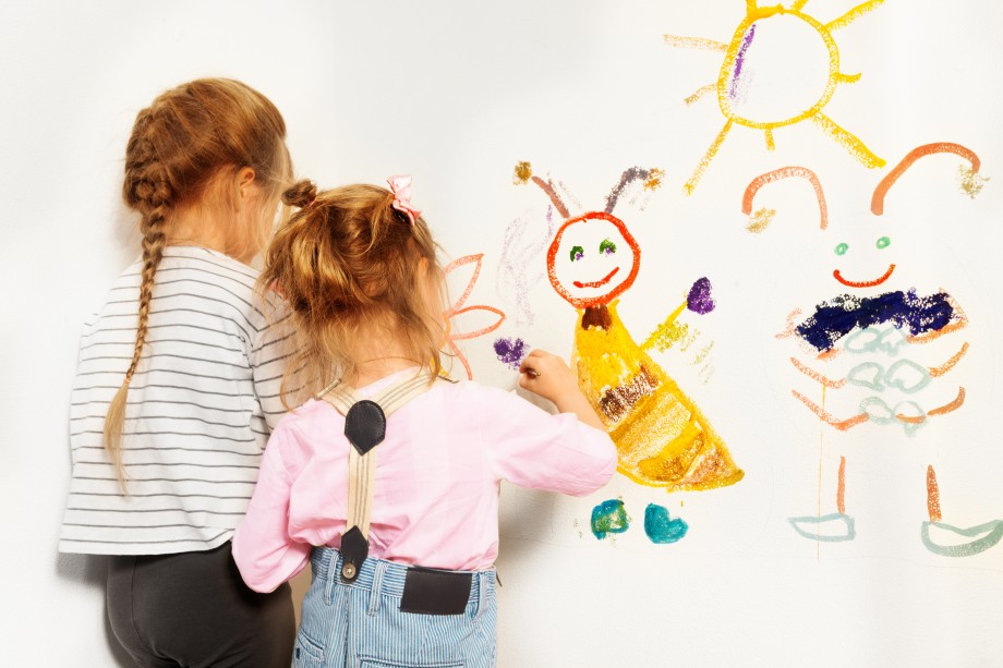 To små jenter står med ryggen til og maler på en vegg