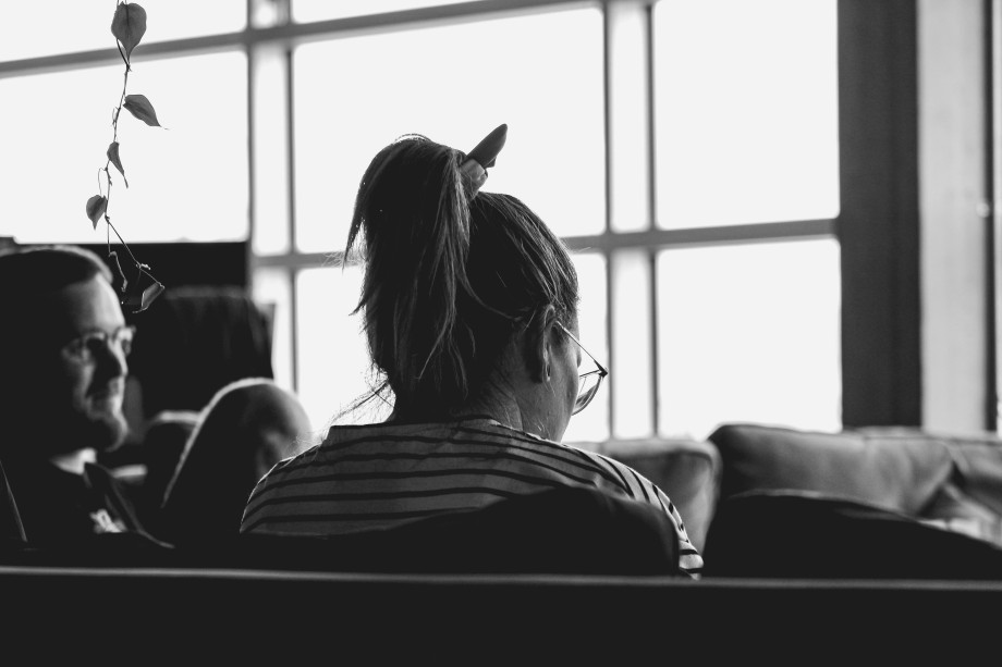 Sort-hvitt bilde av en mann og dame som sitter i sofa og snakker. Damen har ryggen til. Foto.