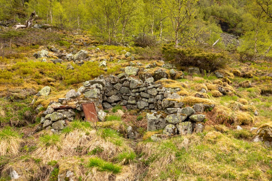 Fig. 3. Kvadratisk tuft som grenser til steinura i en bakkehelling. Den ødelagte ovnen er fra hytta like ved og har ikke sammenheng med tufta. Foto: Andreas Holkestad Sunde   