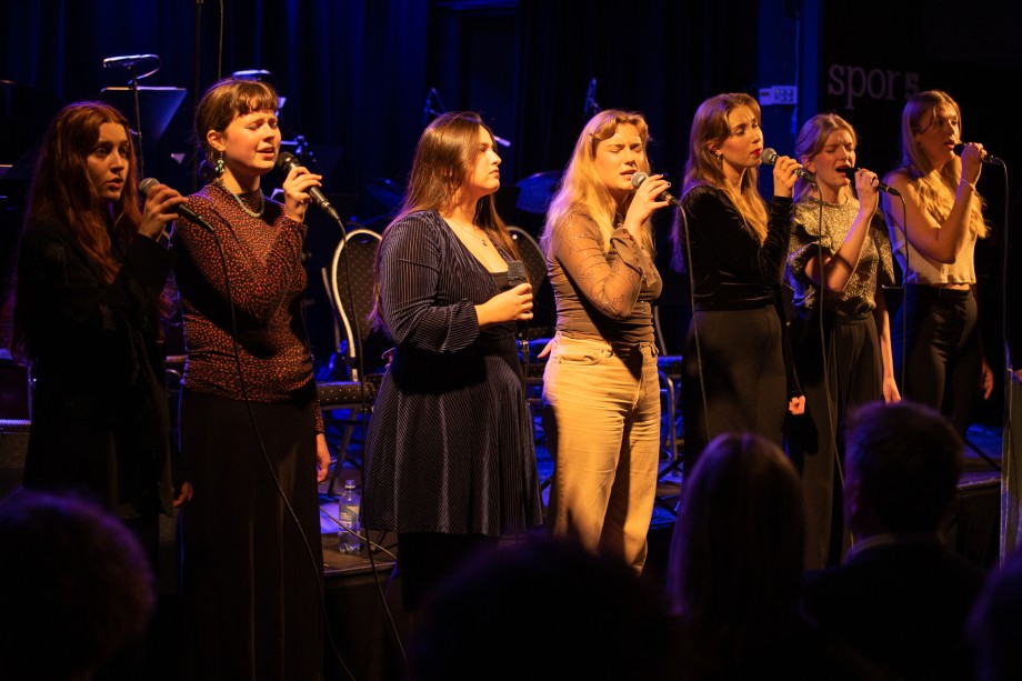 Syv kvinnelige sangstudenter på rekke som synger