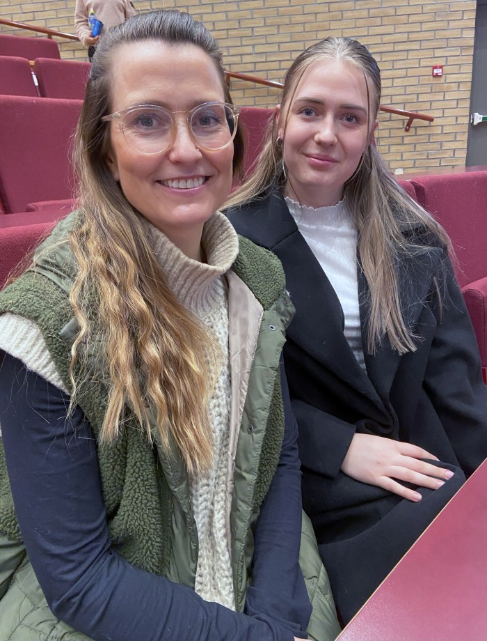 To smilende kvinnelige studenter i et auditorium.