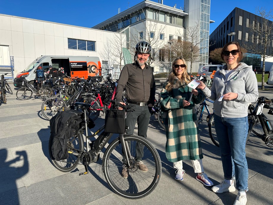 Tre personer foran sykler som er parkert