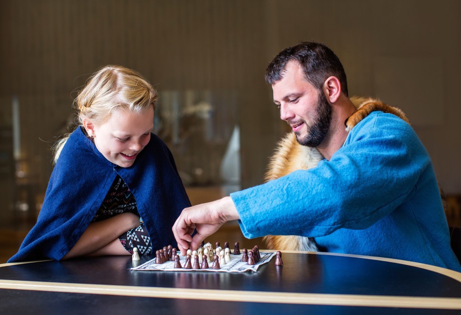 Et barn og en voksen kledd i vikingkapper spiller et gammelt sjakkspill