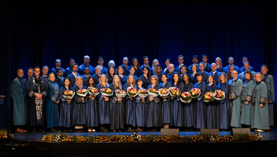 Gruppefoto av rundt 40 kvinner og menn kledt i høytidelige akademiske kapper og med blomsterbuketter.