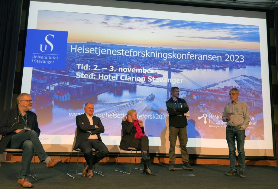 Tre personer i et panel og to ledere av paneldebatt på en scene