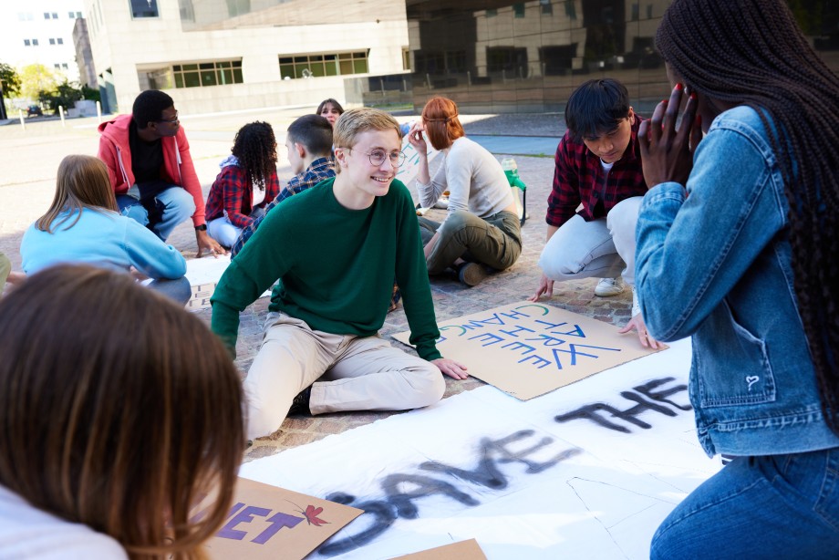 Elever sitter på bakken ute og lager plakater med slagord
