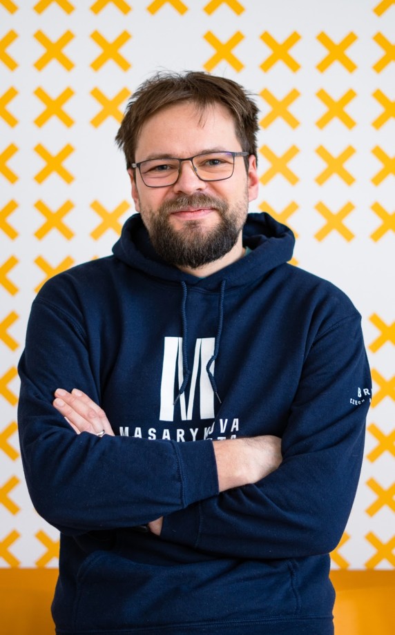 Man with arms crossed in front of a white wall with yellow crosses