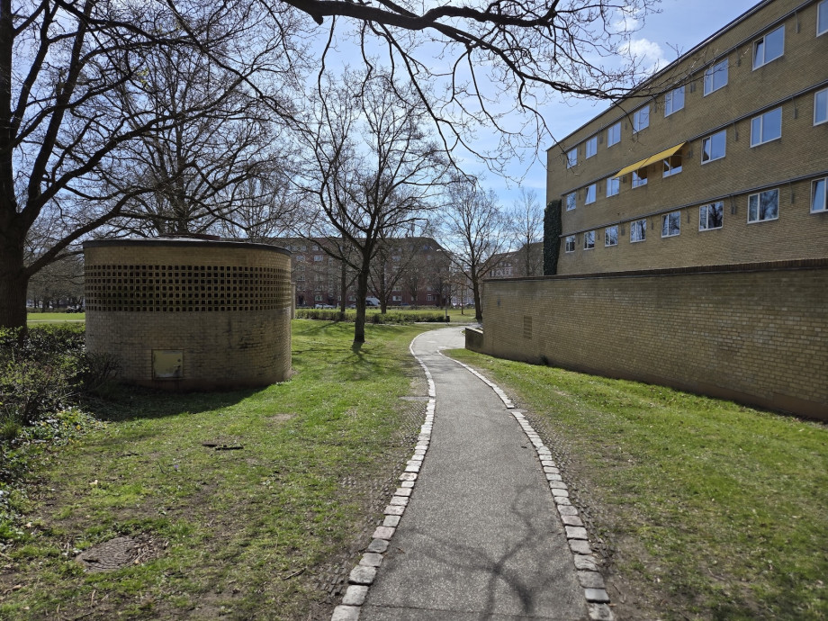 A concrete path flanked by green lawns leads between square buildings and past them