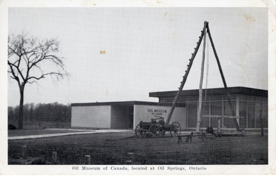 A black and white photograph postcard of a view of the Oil Museum of Canada. The museum is a low building with a flat roof. A single tree stands to the left side of the building.