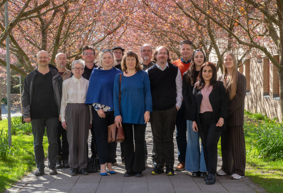 A group of people stand posing for the camera under cherry trees that are in full pink blossom