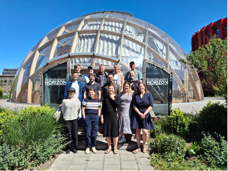 A group of people stand in front of a small, glass, dome-shaped building in a garden