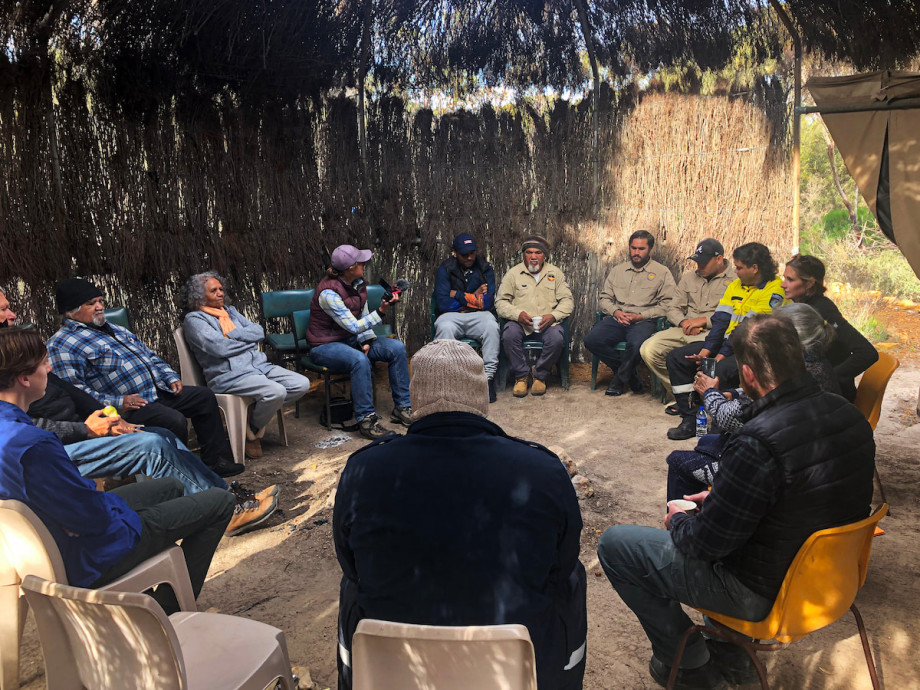 A group of people sit in a circle in a hut