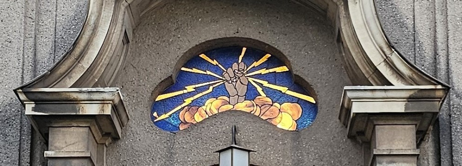 A stained glass window with a fistreaching up out of a cloud. The fist is holding eight bolts of lightning