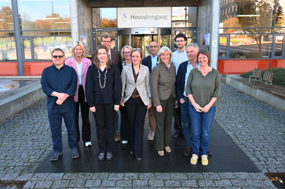 Gruppebilde av menn og kvinner foran en bygning med skilt hvor det står "Universitetet i Stavanger"