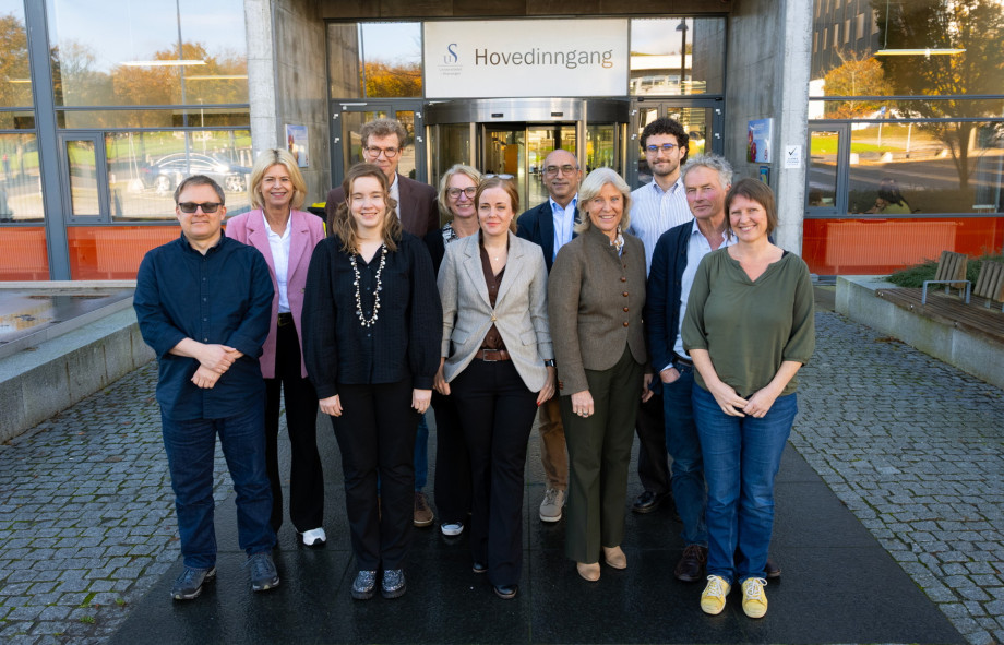 Gruppebilde av menn og kvinner foran en bygning med skilt hvor det står "Universitetet i Stavanger"