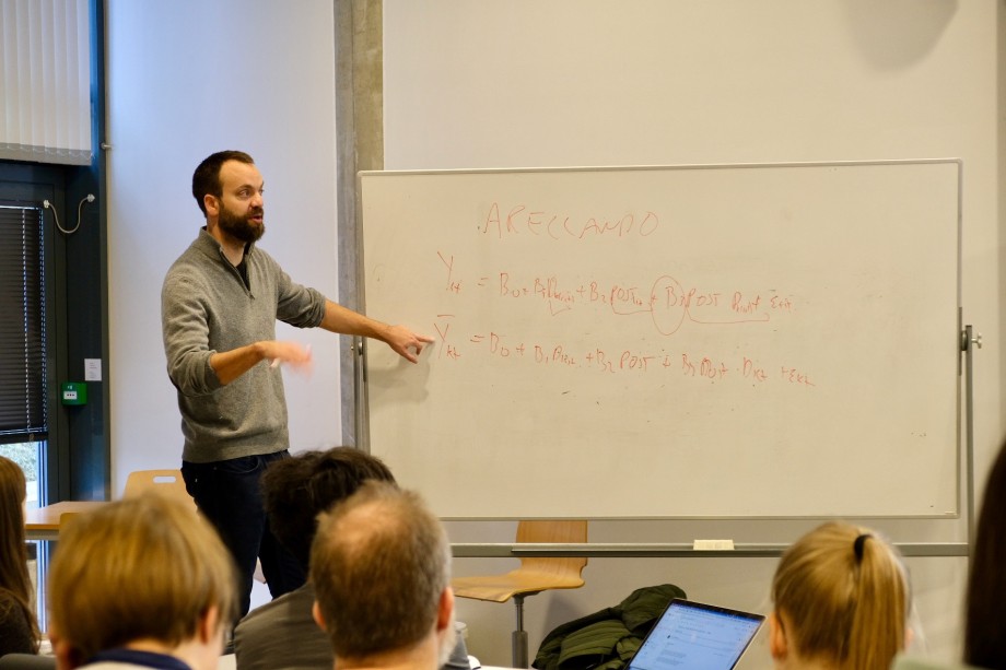 Professor i samfunnsøkonomi underviser PhD-studenter i økonometri i auditorium og tegner ligninger på tavle.