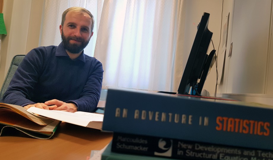 UiS-stipendiat Lukasz Derdowski sitter på kontoret med statistikkbøker foran seg.