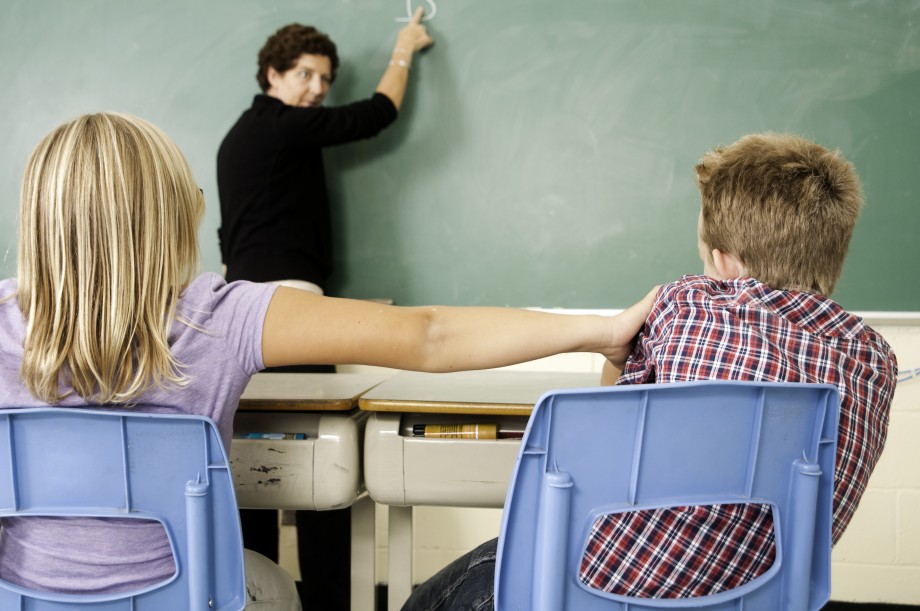 En klasseromssituasjon der en elev dytter en annen. Læreren snur seg fra tavla og oppdager hva som foregår.