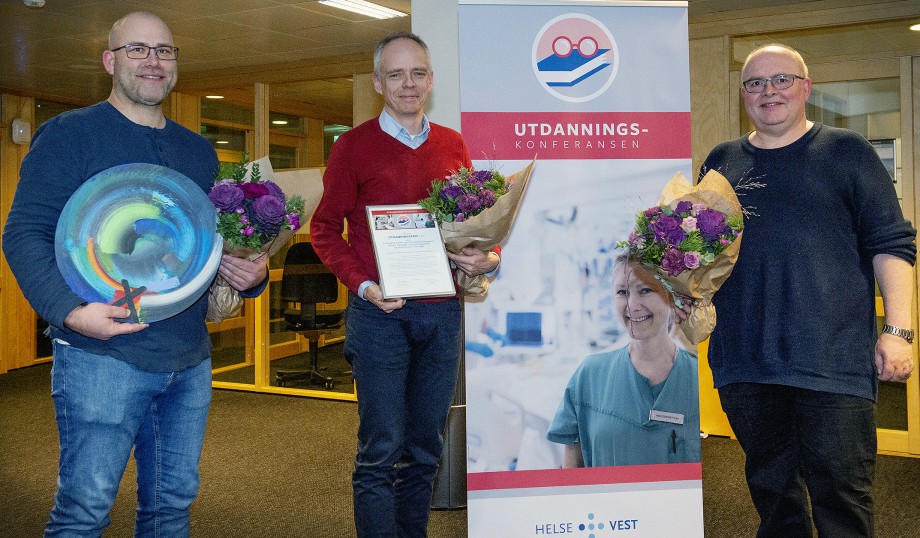 Tre menn (Frode Bremseth, Stephen Sollid og Olav Østebø) står foran en roll-up med teksten Utdanningskonferansen. De holder blomster og et keramikkfat og smiler.