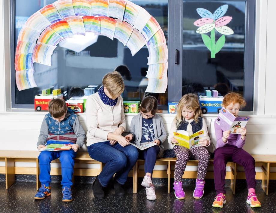 Elever sitter på en benk på skolen og leser sammen med en kvinnelig lærer.