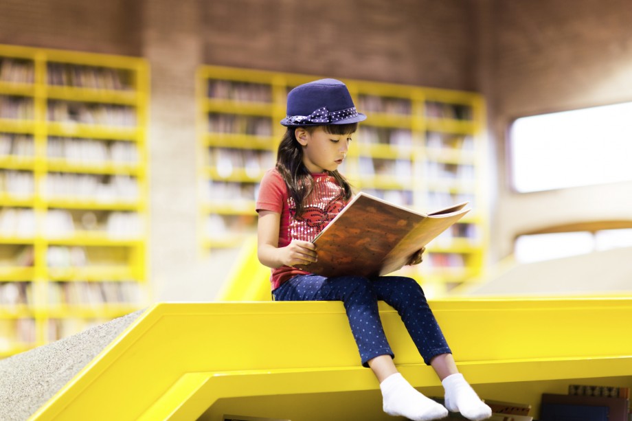 Jente i seksårsalderen sitter i et bibliotek og leser.